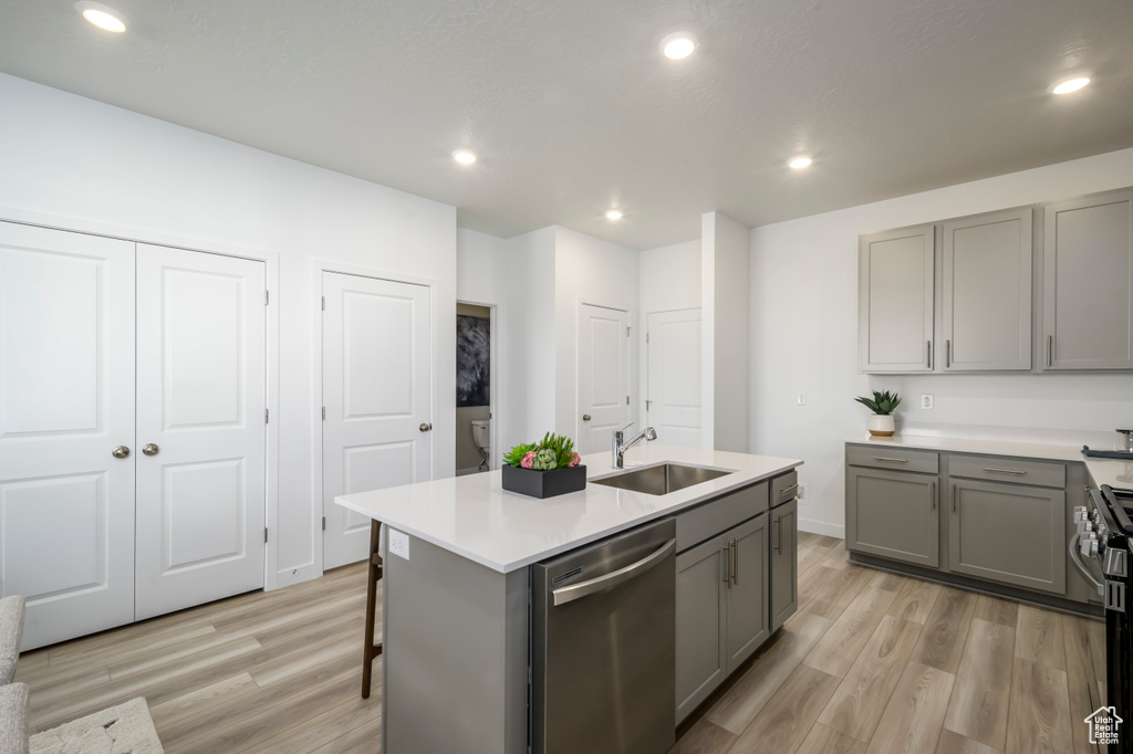 Kitchen featuring light countertops, light wood-type flooring, gray cabinetry, a sink, and dishwasher
