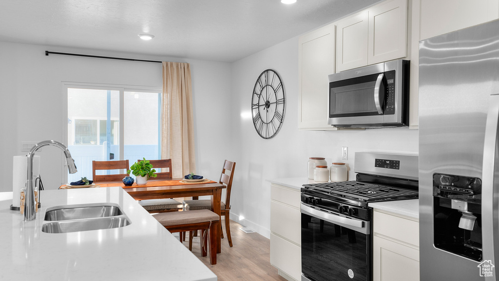 Kitchen featuring white cabinetry, light countertops, light wood-type flooring, a sink, and appliances with stainless steel finishes