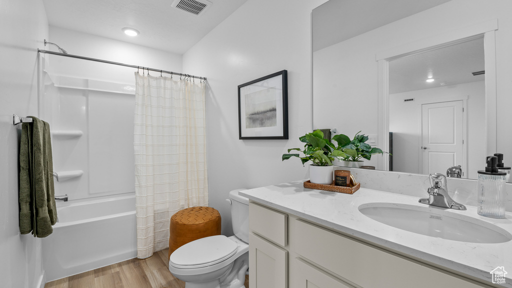 Full bathroom with vanity, shower / tub combo, toilet, visible vents, and wood finished floors