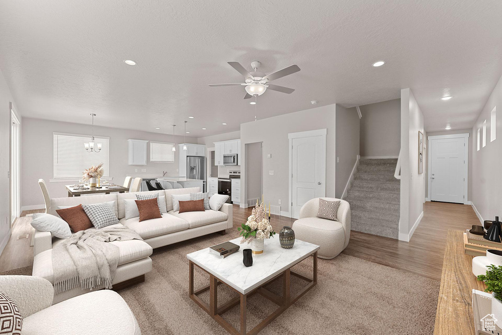 Living area with recessed lighting, light wood-style flooring, ceiling fan with notable chandelier, and stairway
