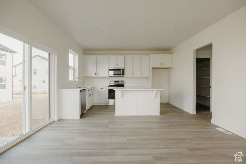 Kitchen with white cabinets, stainless steel appliances, a center island, and light wood-type flooring