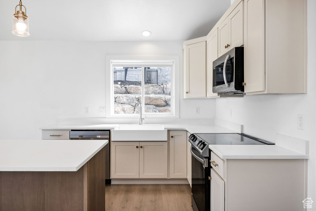 Kitchen with light countertops, a sink, pendant lighting, light wood-style flooring, and appliances with stainless steel finishes