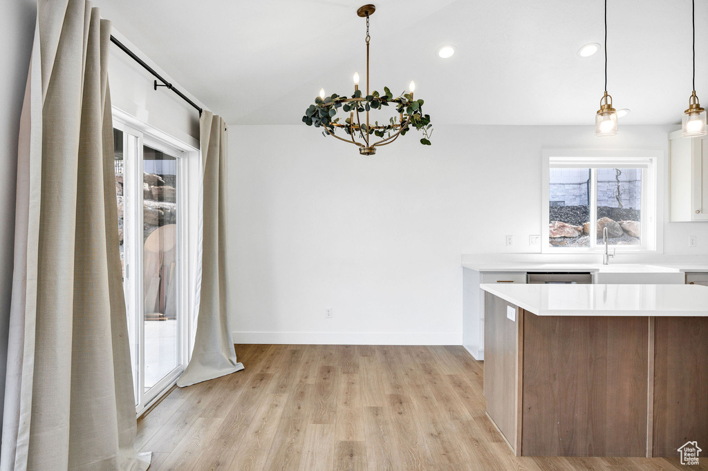 Kitchen with light countertops, white cabinets, a chandelier, light wood-type flooring, and decorative light fixtures