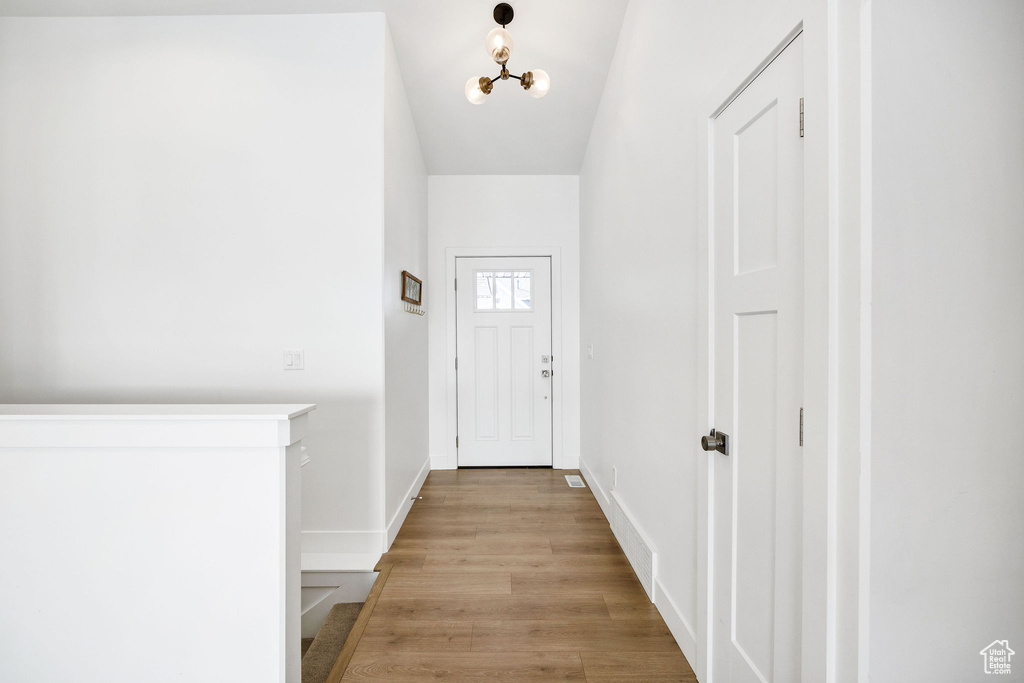 Doorway to outside featuring baseboards, light wood-style flooring, and an inviting chandelier