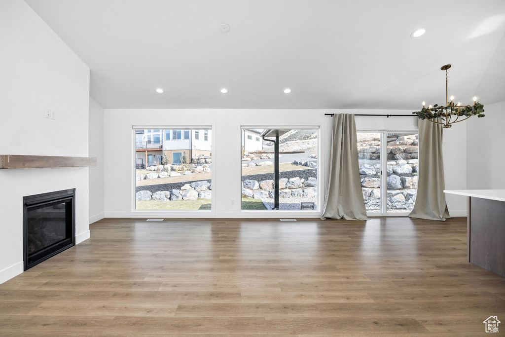 Unfurnished living room with a wealth of natural light, wood finished floors, recessed lighting, and an inviting chandelier