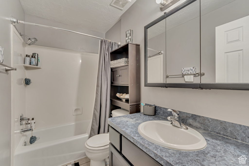 Full bath featuring a textured ceiling, visible vents, toilet, vanity, and shower / tub combo