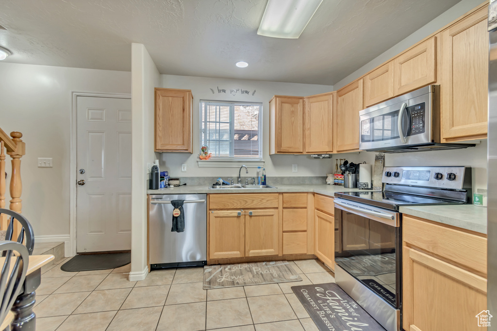 Kitchen with light tile patterned flooring, light countertops, a sink, light brown cabinetry, and appliances with stainless steel finishes