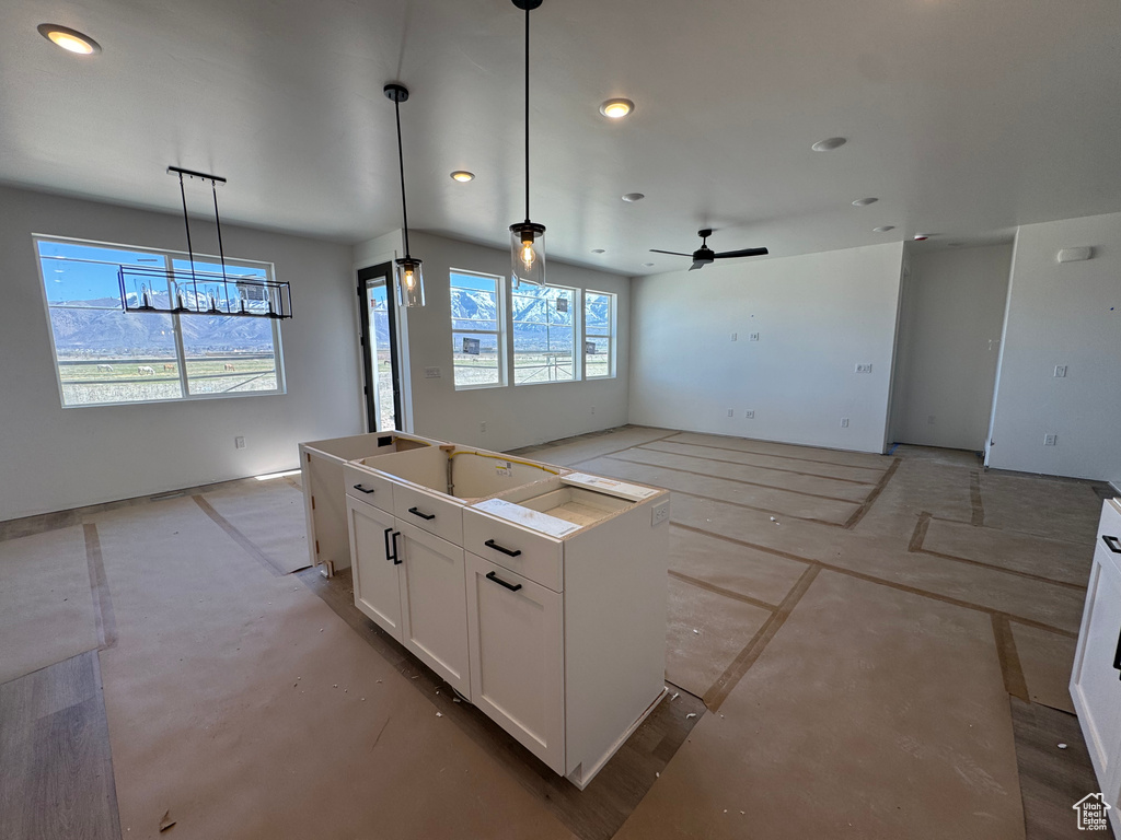Kitchen featuring pendant lighting, a kitchen island, open floor plan, white cabinets, and ceiling fan