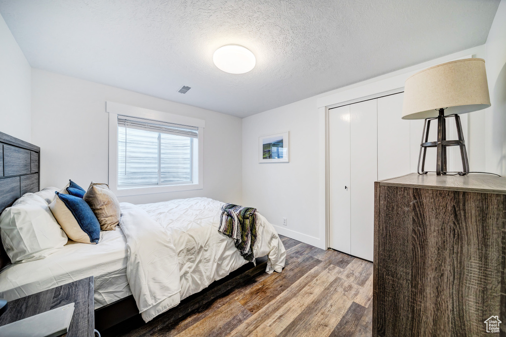 Bedroom with baseboards, a textured ceiling, visible vents, a closet, and wood finished floors