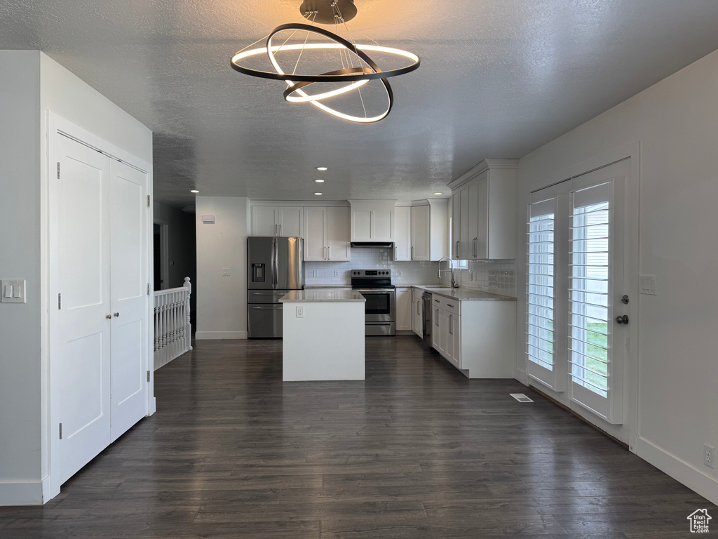 Kitchen featuring dark wood finished floors, a center island, appliances with stainless steel finishes, light countertops, and a sink