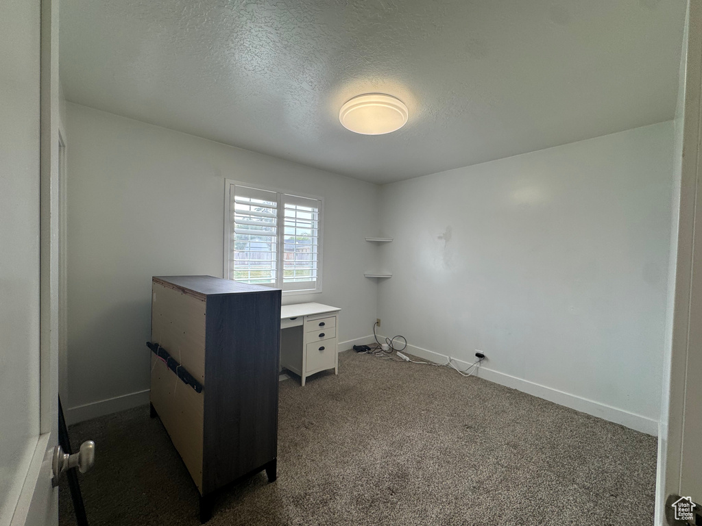Unfurnished office with dark carpet, a textured ceiling, and baseboards