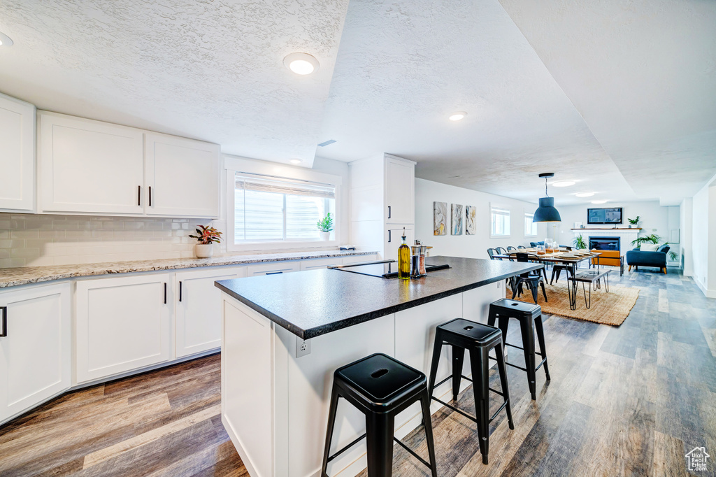 Kitchen featuring a breakfast bar, white cabinets, wood finished floors, and tasteful backsplash