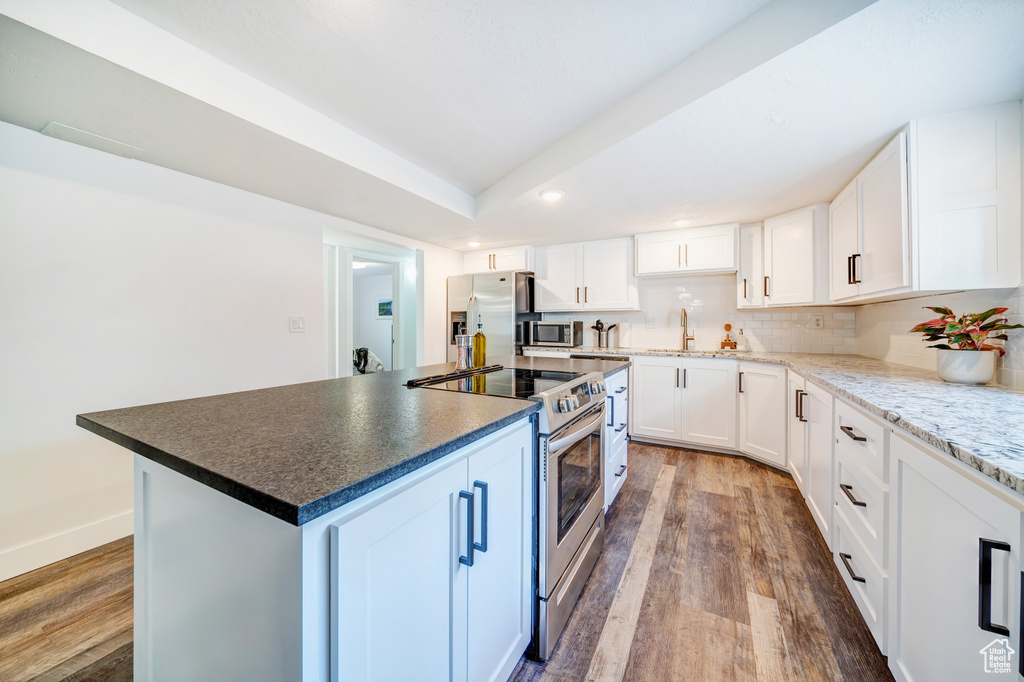 Kitchen with a sink, wood finished floors, decorative backsplash, and appliances with stainless steel finishes