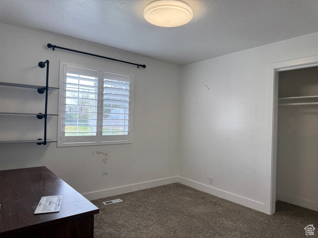 Unfurnished bedroom with dark carpet, baseboards, and visible vents