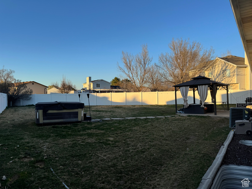 View of yard with a hot tub, central air condition unit, a fenced backyard, and a gazebo