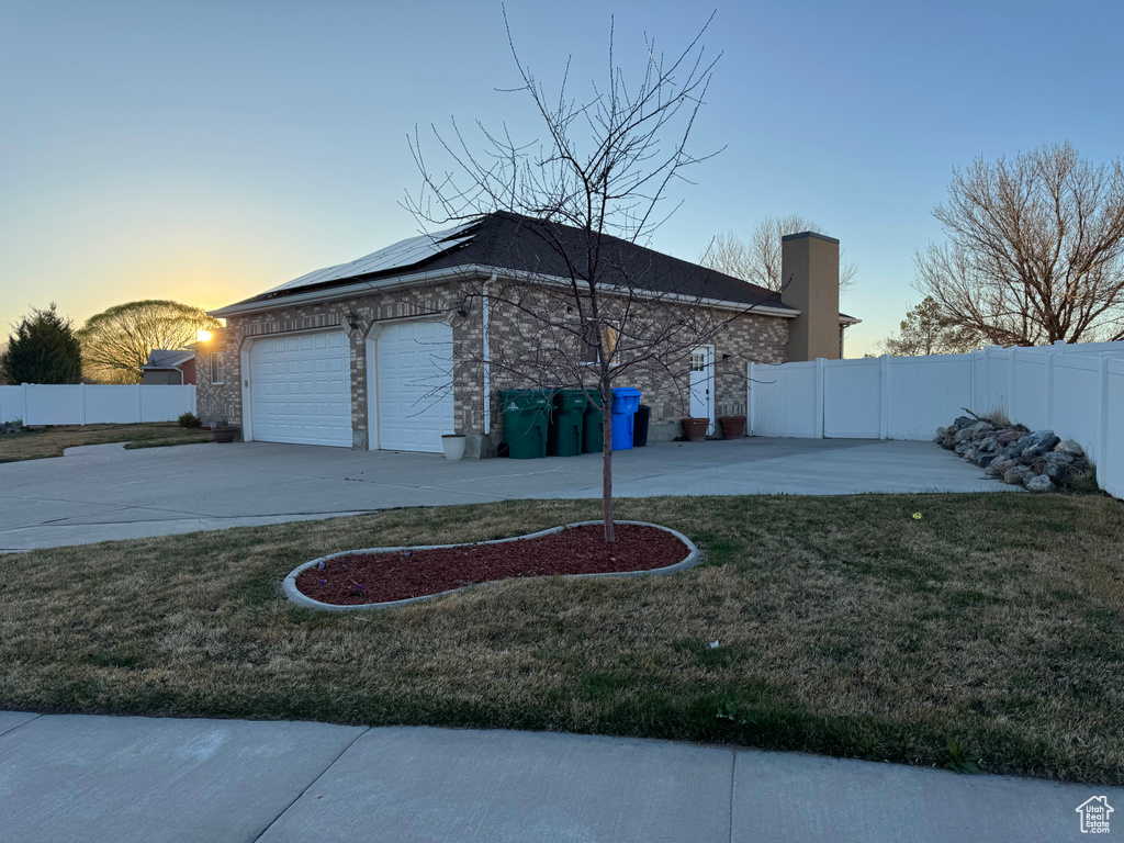 View of side of property with fence, solar panels, a yard, and an attached garage