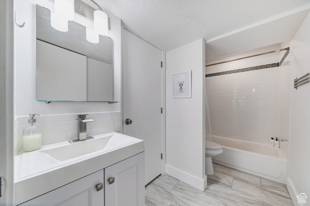 Full bathroom with vanity, toilet, baseboards, a textured ceiling, and backsplash
