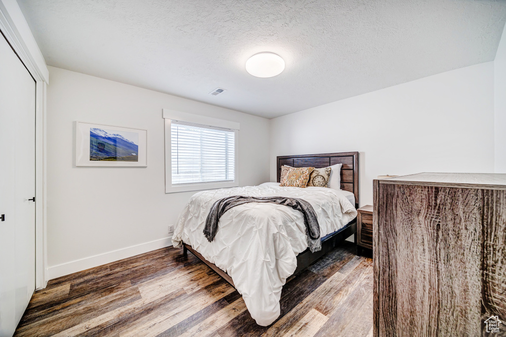 Bedroom featuring baseboards, a textured ceiling, visible vents, and wood finished floors