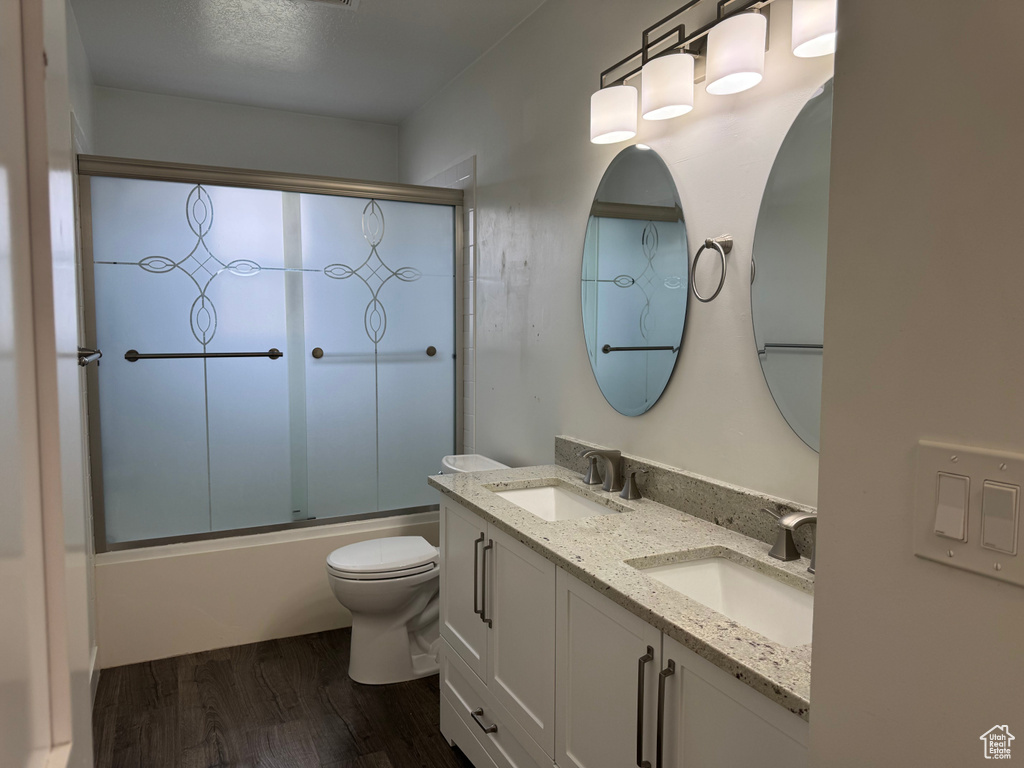 Full bath featuring combined bath / shower with glass door, a sink, toilet, and wood finished floors