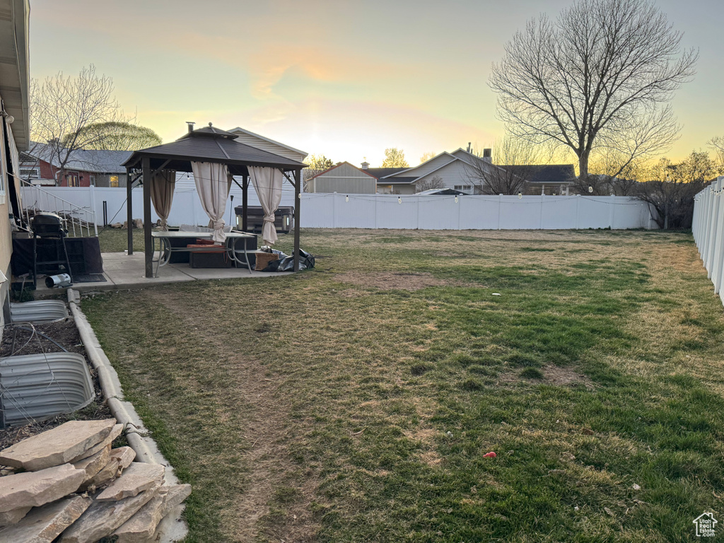 Yard at dusk featuring a fenced backyard, an outdoor hangout area, a gazebo, and a patio area
