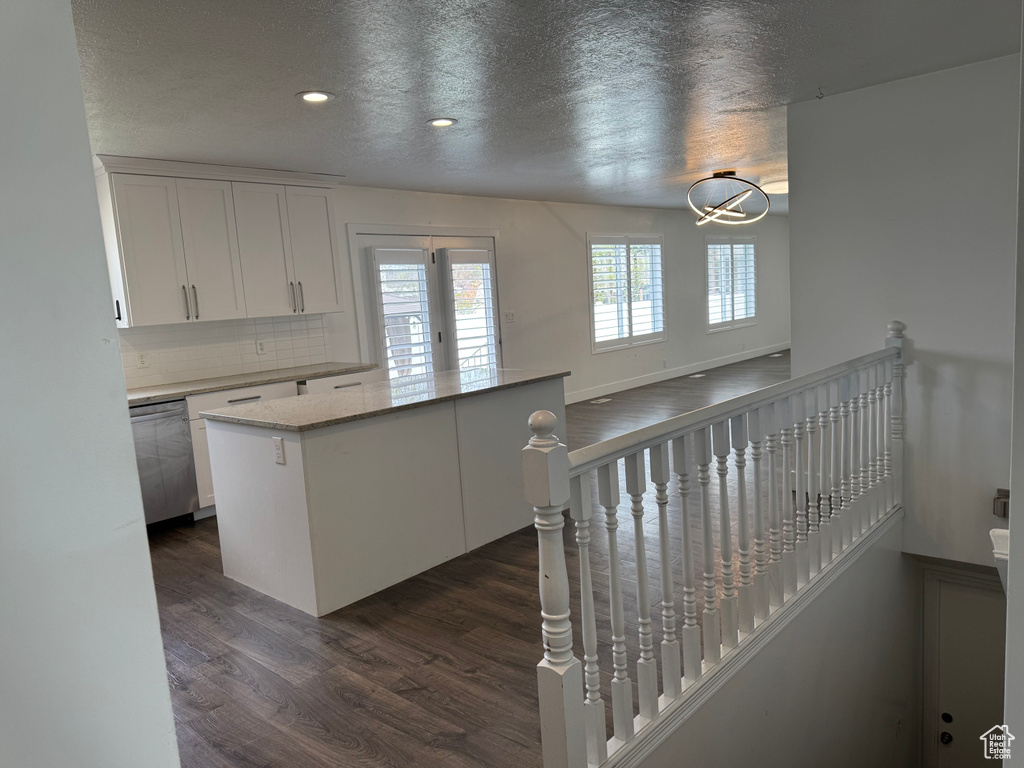Kitchen featuring dark wood-style flooring, white cabinets, stainless steel dishwasher, and a wealth of natural light
