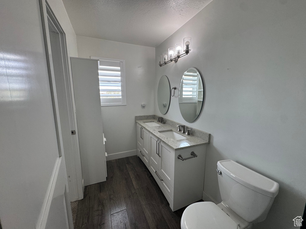 Bathroom with a textured ceiling, a sink, toilet, and wood finished floors