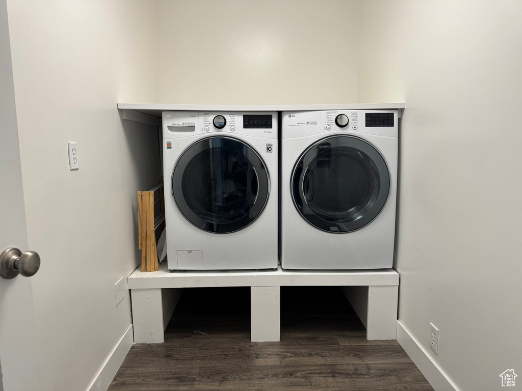 Clothes washing area featuring dark wood-type flooring, washing machine and clothes dryer, laundry area, and baseboards
