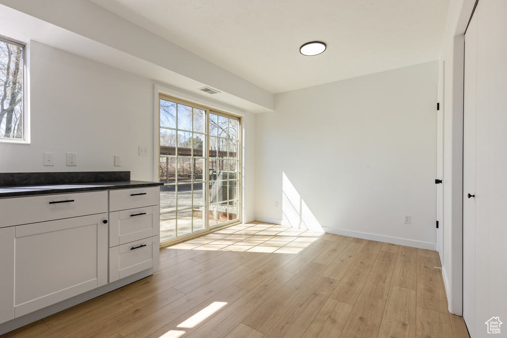 Unfurnished dining area featuring baseboards, light wood-type flooring, and visible vents