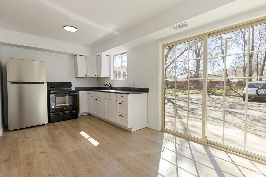 Kitchen featuring black / electric stove, a sink, dark countertops, visible vents, and freestanding refrigerator