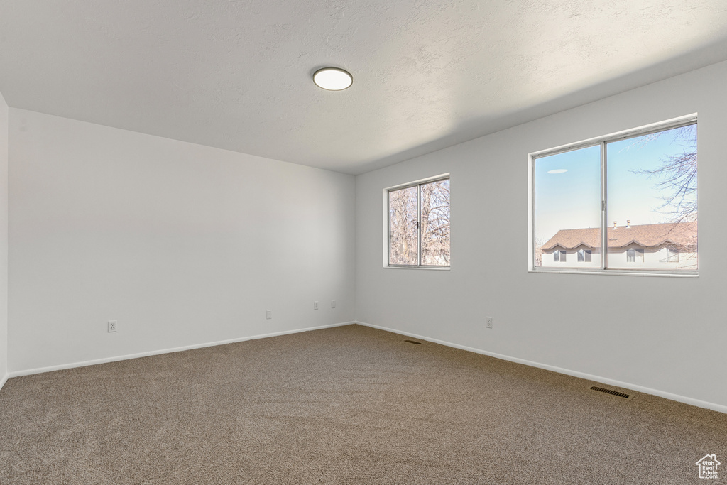 Unfurnished room featuring carpet, baseboards, a textured ceiling, and visible vents