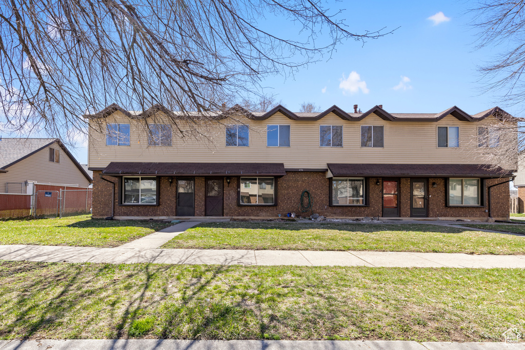 Townhome / multi-family property with a front lawn, fence, and brick siding