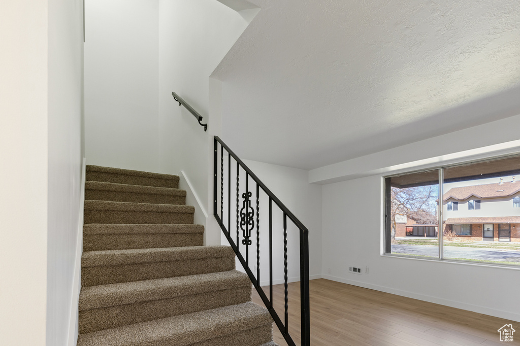 Staircase featuring visible vents, a textured ceiling, baseboards, and wood finished floors