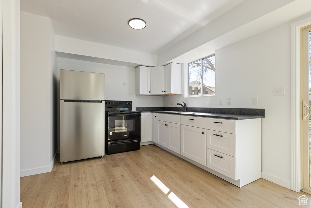 Kitchen with freestanding refrigerator, light wood finished floors, black electric range oven, dark countertops, and white cabinets