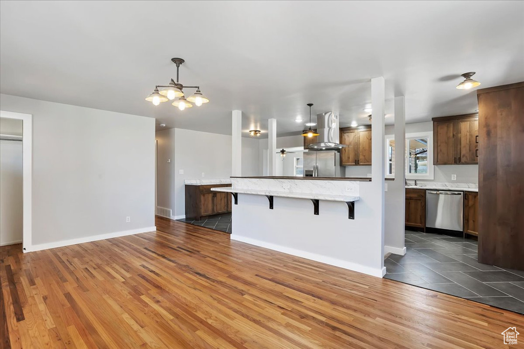 Kitchen with a chandelier, wood finished floors, a breakfast bar, appliances with stainless steel finishes, and wall chimney range hood