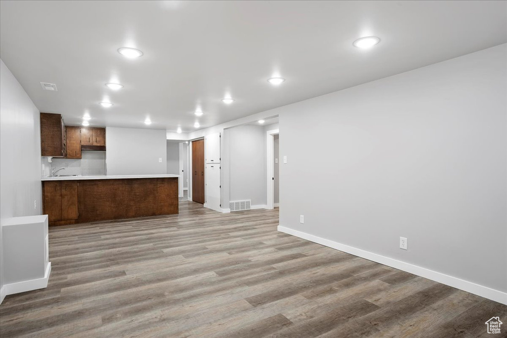 Unfurnished living room featuring a sink, baseboards, light wood-style floors, and recessed lighting