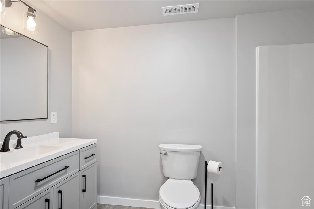 Bathroom featuring vanity, toilet, baseboards, visible vents, and wood finished floors