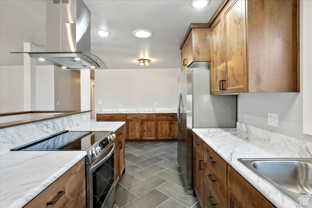 Kitchen featuring island exhaust hood, brown cabinets, recessed lighting, stainless steel range with electric cooktop, and a sink
