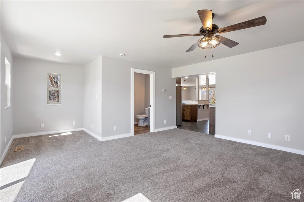 Unfurnished room with baseboards, visible vents, dark carpet, and a ceiling fan