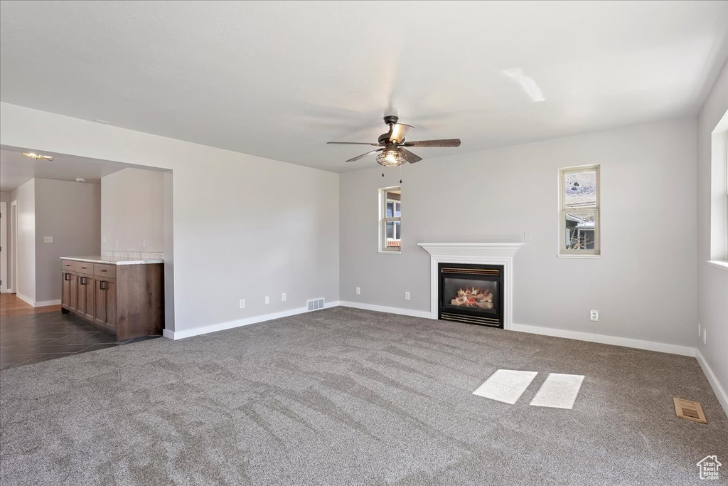 Unfurnished living room with dark colored carpet, baseboards, visible vents, a ceiling fan, and a glass covered fireplace