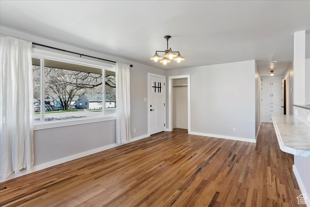 Unfurnished dining area with visible vents, a notable chandelier, baseboards, and wood finished floors