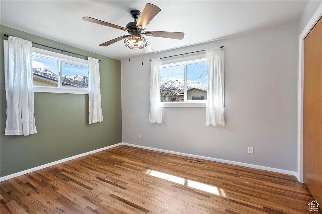 Empty room featuring wood finished floors, baseboards, a healthy amount of sunlight, and visible vents