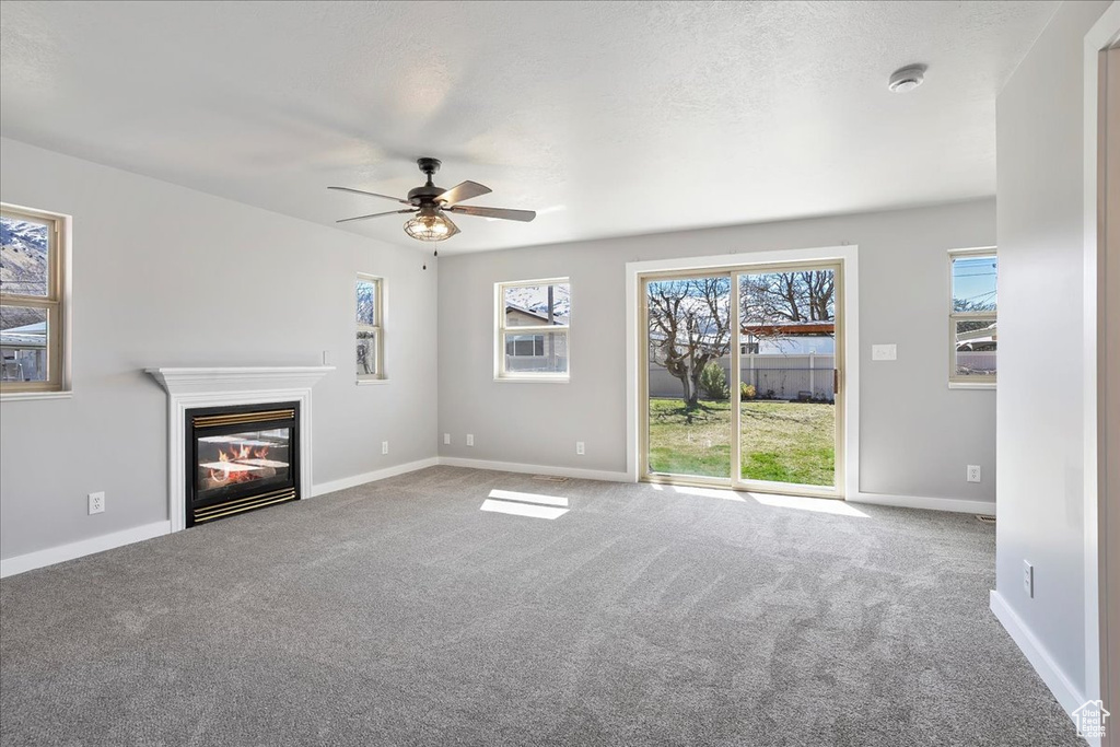 Unfurnished living room featuring a ceiling fan, a glass covered fireplace, a textured ceiling, baseboards, and carpet