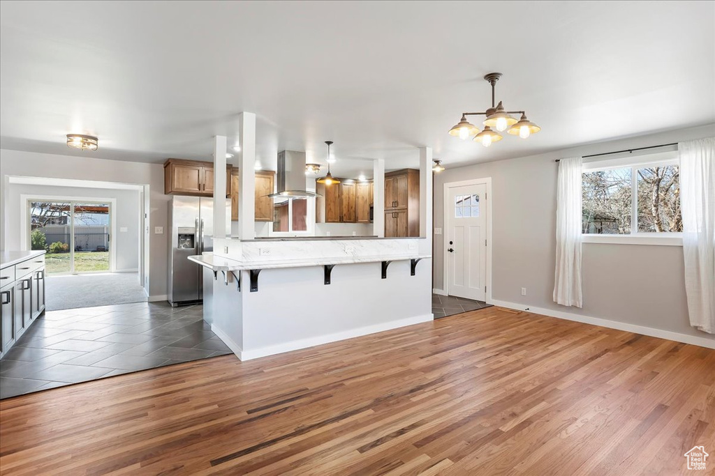 Kitchen with stainless steel fridge, a breakfast bar, wood finished floors, exhaust hood, and brown cabinetry