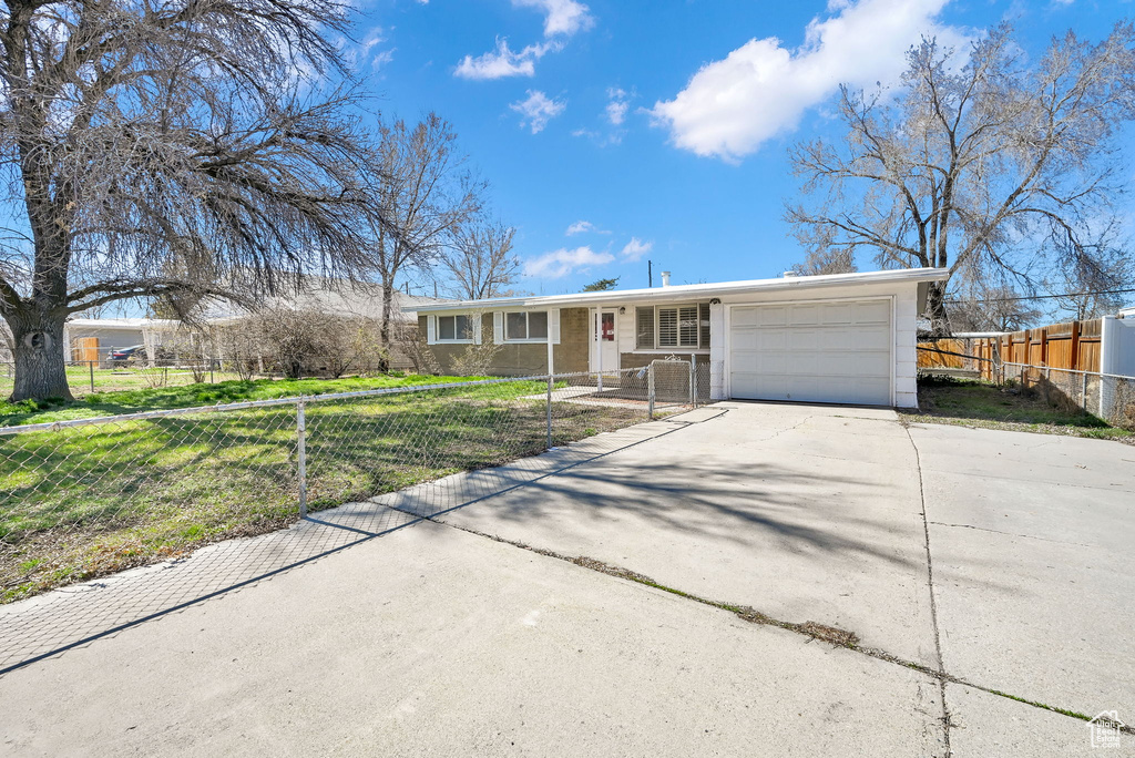 Ranch-style house featuring a garage, concrete driveway, a front yard, and a fenced front yard