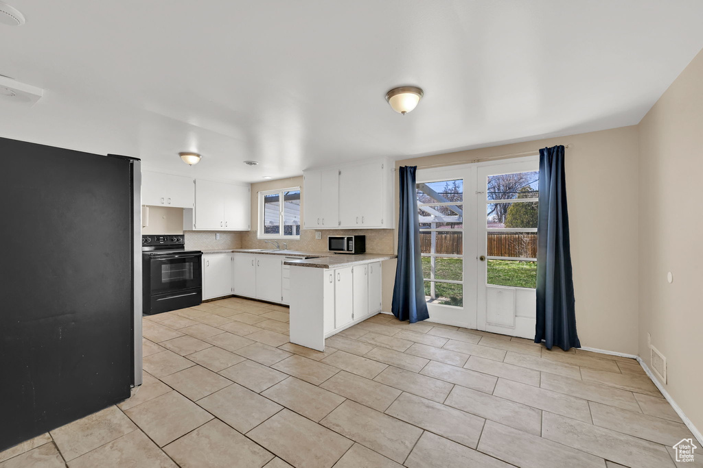 Kitchen featuring stainless steel microwave, black range with electric cooktop, visible vents, freestanding refrigerator, and a peninsula