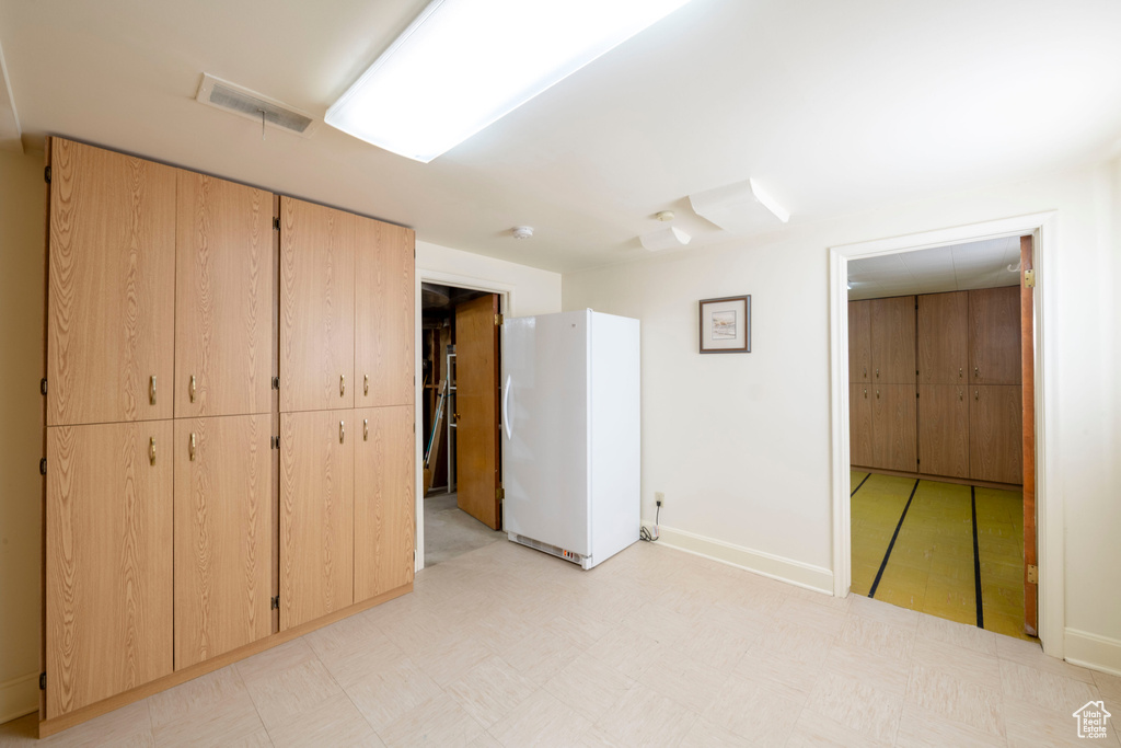 Unfurnished bedroom featuring baseboards, visible vents, light floors, and freestanding refrigerator