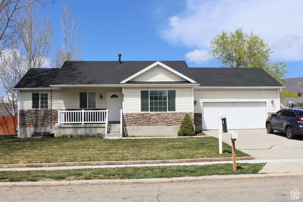 Single story home featuring concrete driveway, stone siding, an attached garage, a porch, and a front lawn