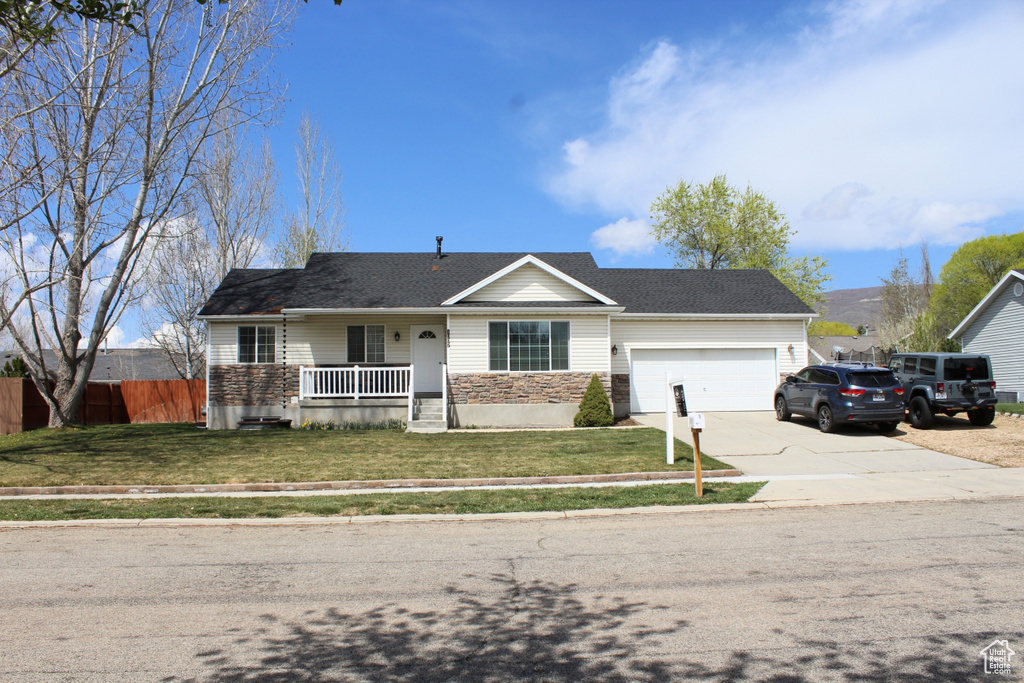 Ranch-style house featuring a porch, a front yard, concrete driveway, an attached garage, and fence