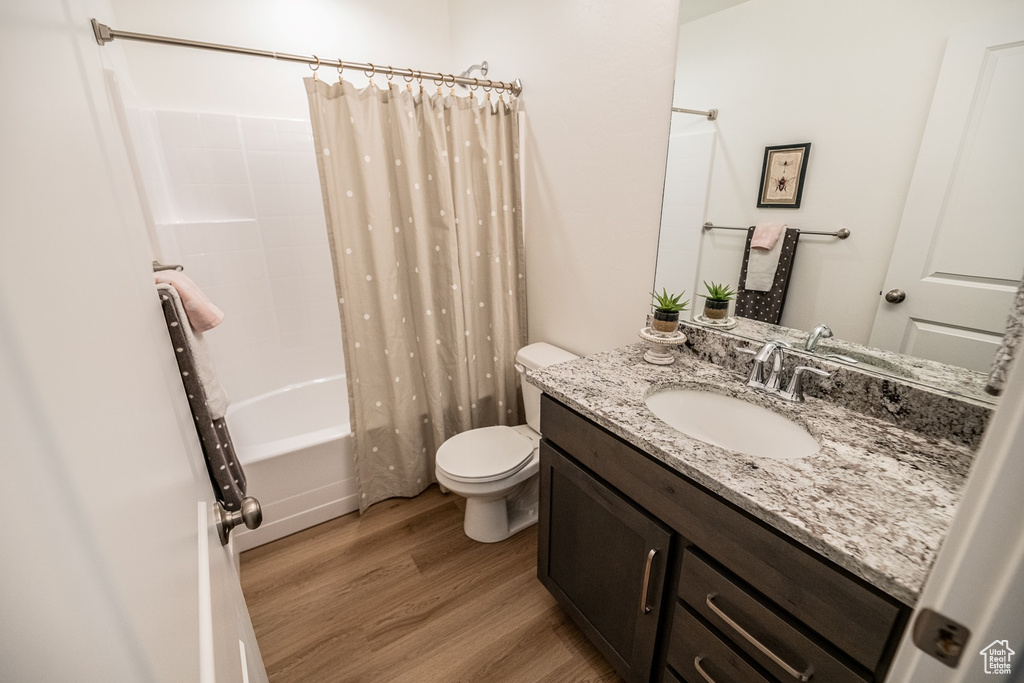 Bathroom featuring wood finished floors, toilet, shower / tub combo, and vanity