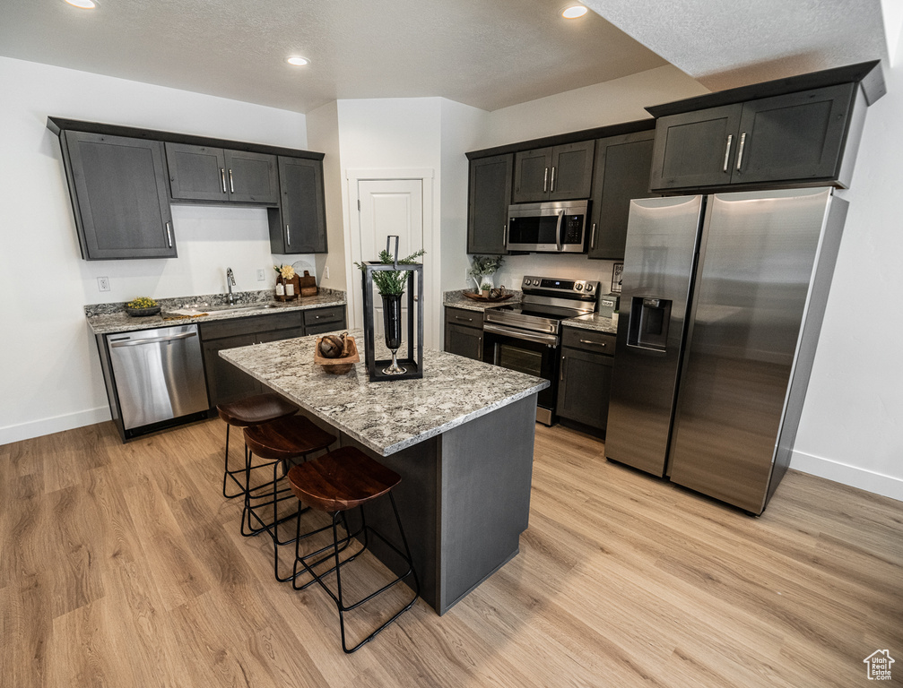 Kitchen featuring a kitchen bar, stainless steel appliances, a center island, light wood-style floors, and light stone countertops